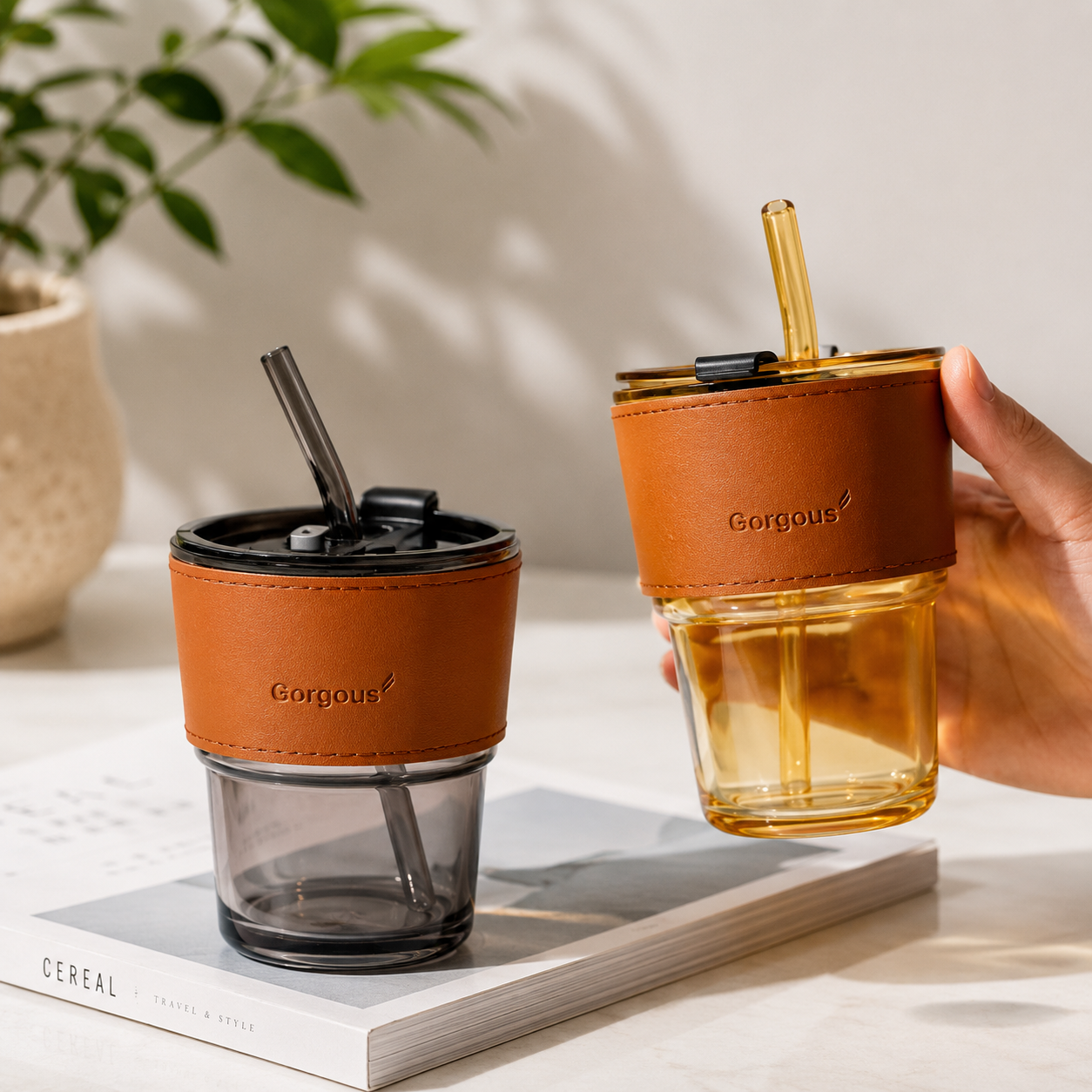 Gold and black aesthetic glass coffee tumblers with reusable straws in lifestyle setup with hand holding tumbler