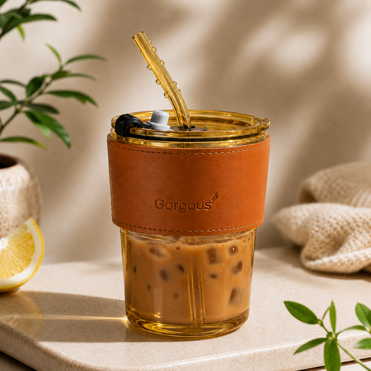 Gold aesthetic glass coffee tumbler with iced coffee, reusable straw, and lid on neutral background