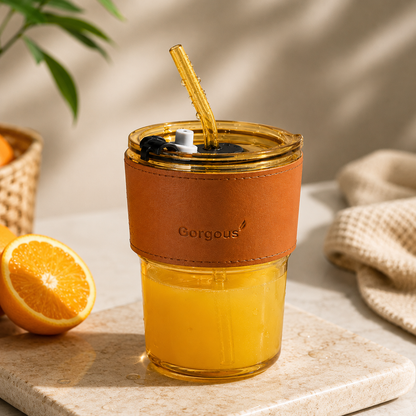 Gold aesthetic glass tumbler filled with orange juice and reusable straw on neutral background